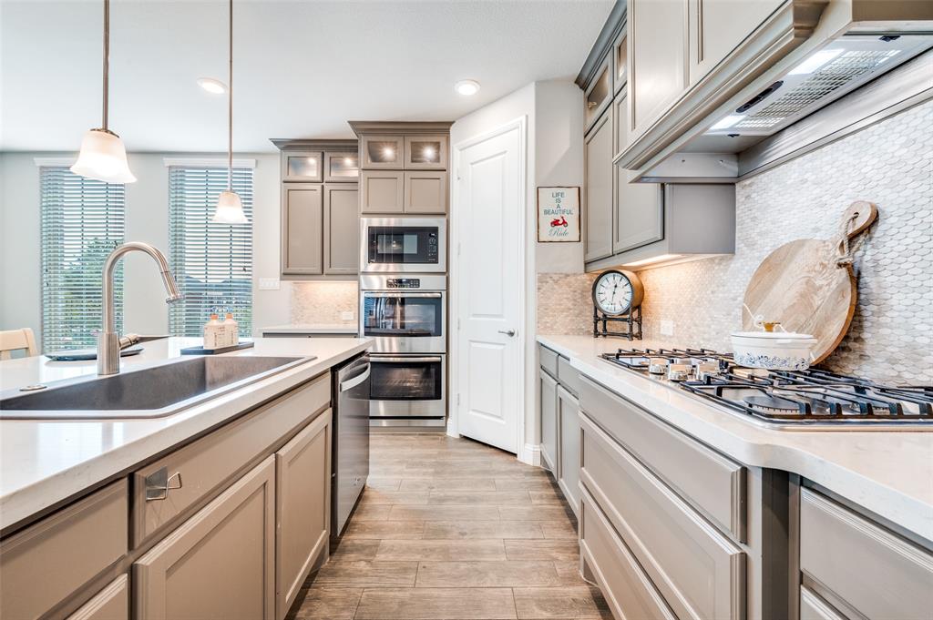 6117 Hall Road Frisco, TX 75034 - Photo 11 of 32 Kitchen featuring gray cabinetry, stainless steel appliances, hanging light fixtures, light wood finished floors, and light stone countertops