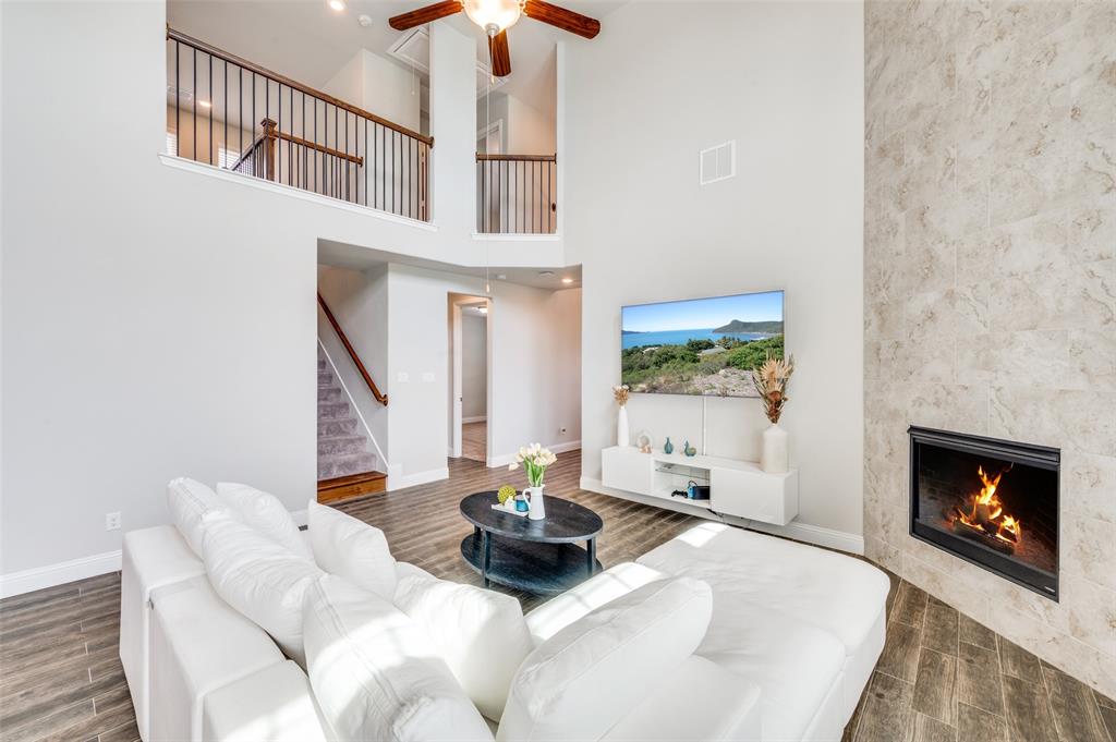 6117 Hall Road Frisco, TX 75034 - Photo 5 of 32 Living room featuring a fireplace, wood tiled floors, ceiling fan, and a high ceiling