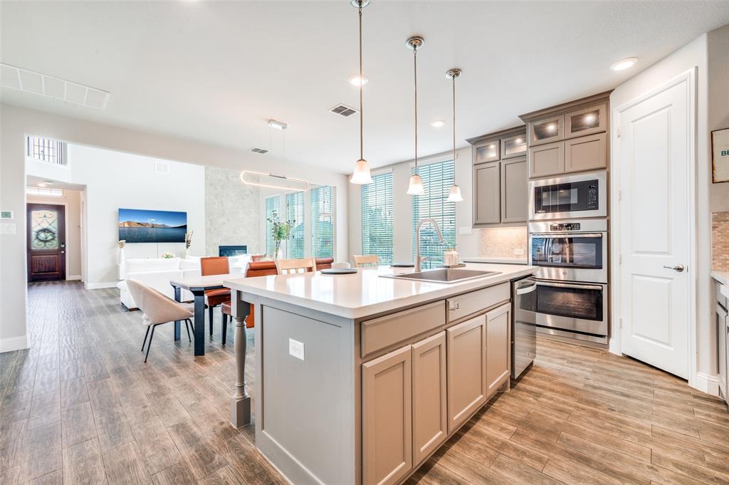 6117 Hall Road Frisco, TX 75034 - Photo 7 of 32 Kitchen with gray cabinetry, an island with sink, a breakfast bar, backsplash, and stainless steel appliances