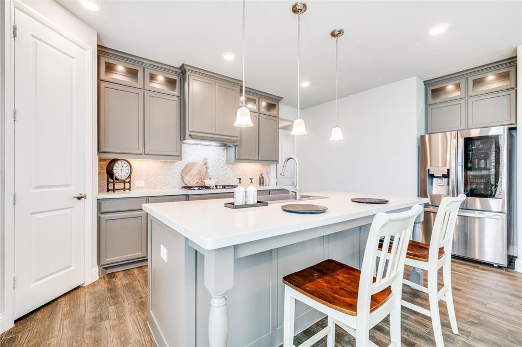 6117 Hall Road Frisco, TX 75034 - Photo 9 of 32 Kitchen featuring gray cabinets, glass insert cabinets, stainless steel fridge, and a kitchen breakfast bar