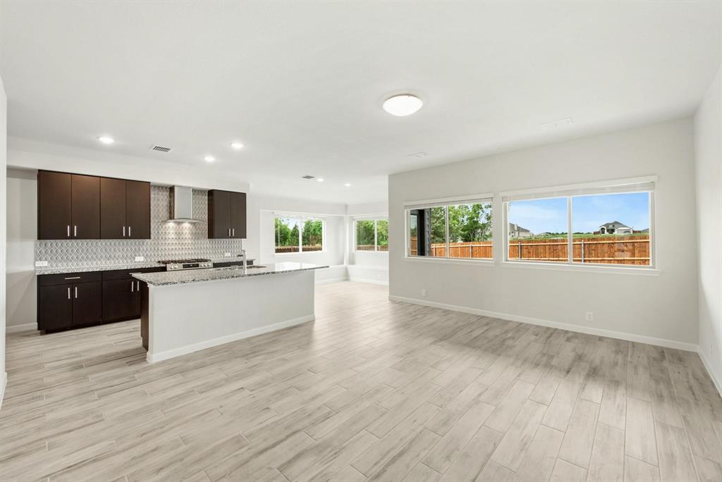 920 Elk Ridge Run Godley, TX 76044 - Photo 19 of 34 Open-concept living space featuring wood-finish flooring, a kitchen island with stone countertop, stainless steel range hood, recessed lighting, and multiple windows