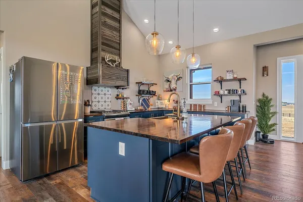 a kitchen with stainless steel appliances granite countertop a sink a refrigerator a kitchen island a stove and a dining table with wooden floor