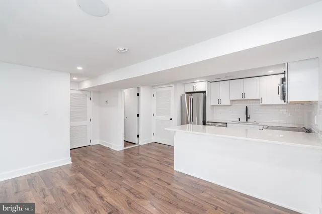 a large white kitchen with kitchen island a sink wooden floor and white stainless steel appliances