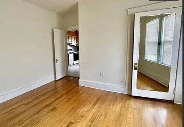 a view of an empty room with wooden floor and a window