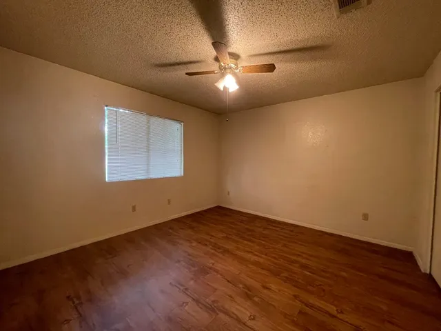 a view of an empty room with wooden floor and a ceiling fan