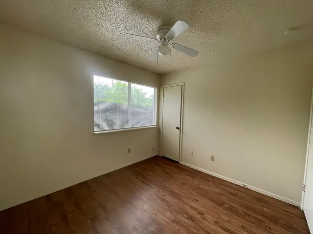 an empty room with wooden floor fan and windows