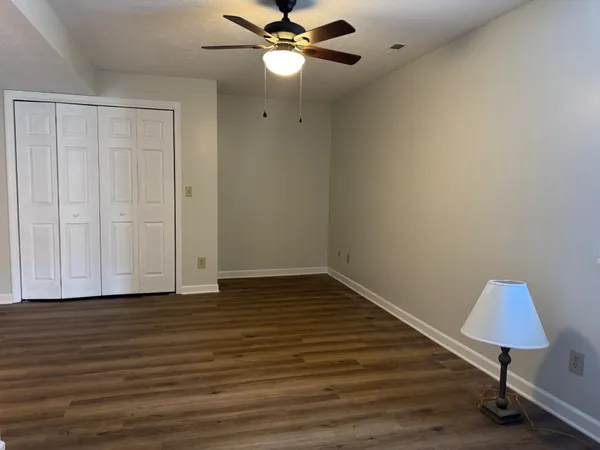 a view of an empty room with wooden floor and a ceiling fan