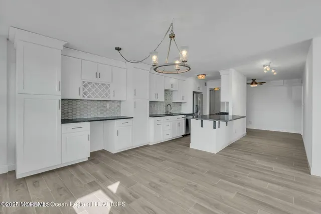 a large kitchen with kitchen island a refrigerator a stove a sink dishwasher and white cabinets with wooden floor