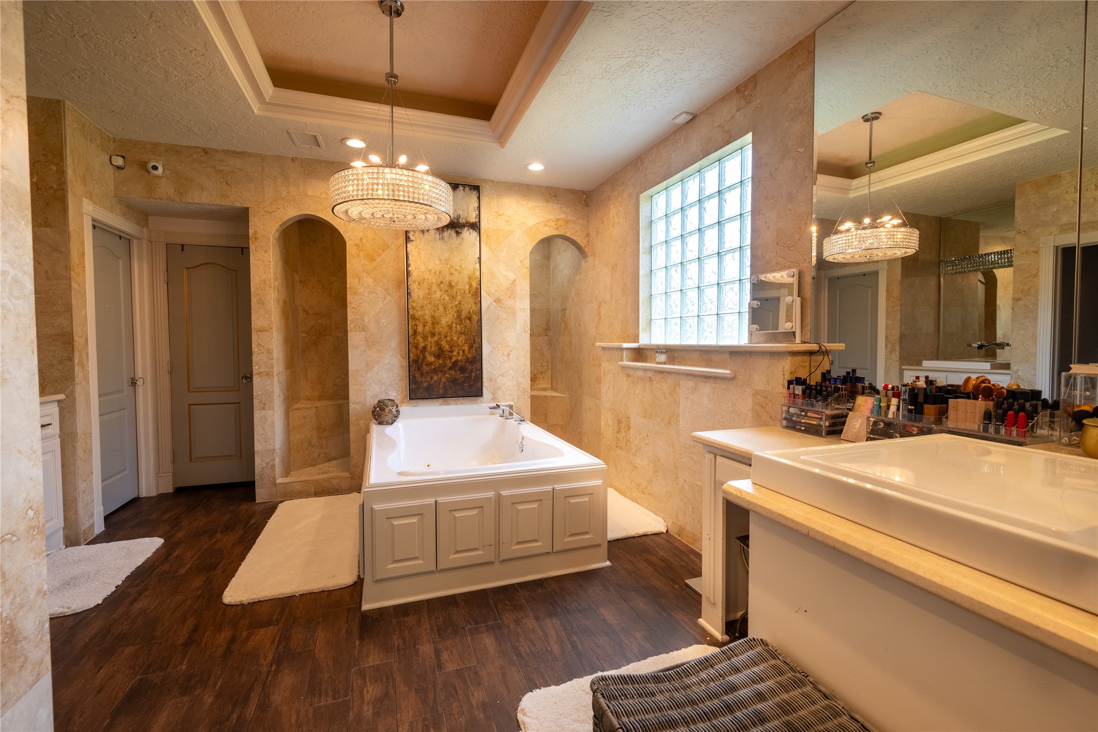 4002 Silver Ridge Boulevard Missouri City, TX 77459 - Photo 20 of 50 This is a spacious bathroom featuring a large tub, dual vanity, separate shower area, wood-look flooring, and ample natural light from the glass block window. A chandelier adds a touch of elegance.