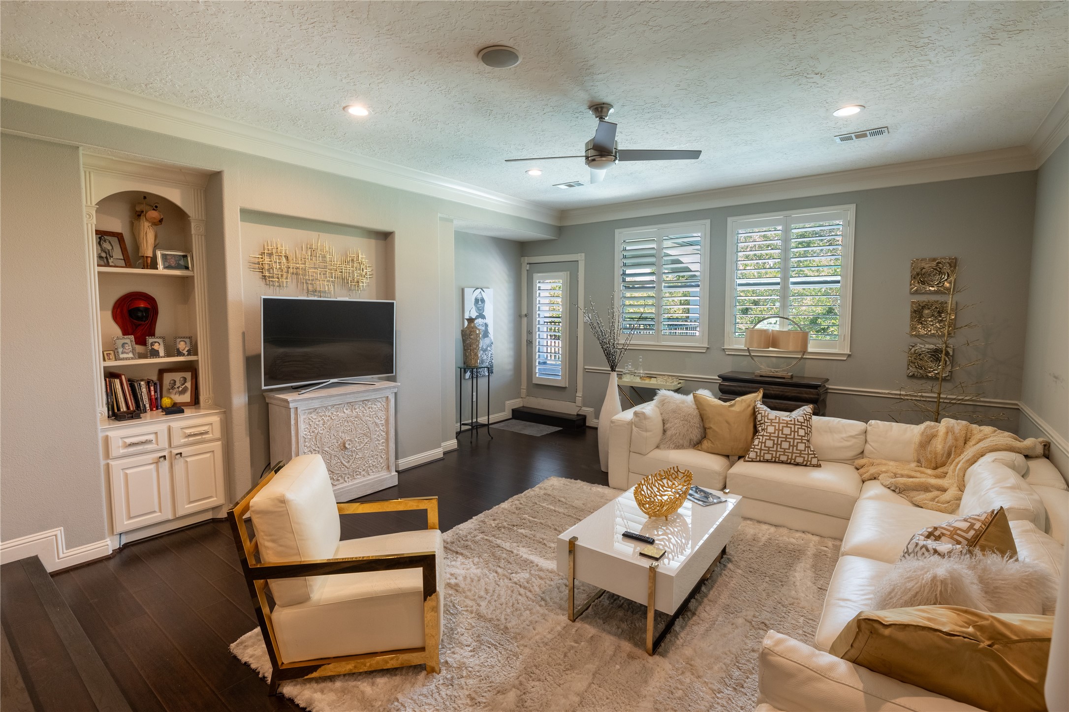 4002 Silver Ridge Boulevard Missouri City, TX 77459 - Photo 28 of 50 This is a spacious and well-lit Gameroom room with elegant dark hardwood floors, built-in shelving, and plantation shutters on the windows. The room is styled with a large, comfortable sectional sofa, a modern accent chair, and a sleek coffee table, creating a cozy and stylish space.