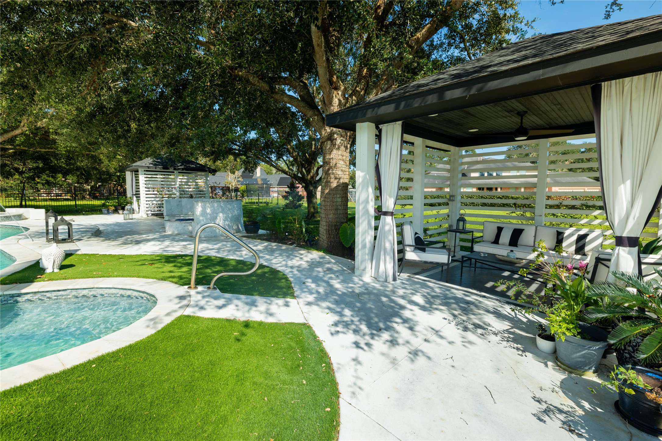 4002 Silver Ridge Boulevard Missouri City, TX 77459 - Photo 39 of 50 This is an elegant outdoor space featuring a swimming pool with a curved entry and handrail, a covered patio area with comfortable seating, surrounded by lush greenery and mature trees, offering a perfect blend of relaxation and entertainment possibilities.