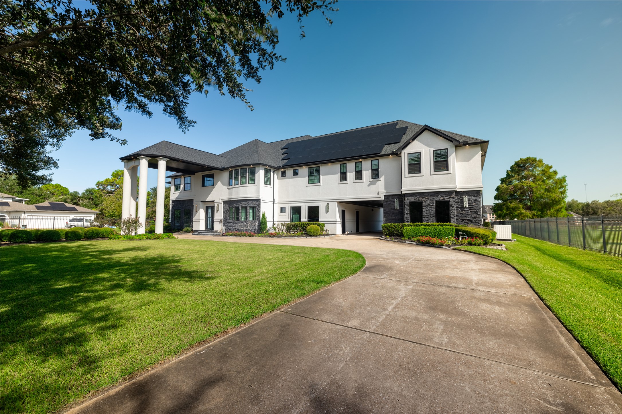 4002 Silver Ridge Boulevard Missouri City, TX 77459 - Photo 4 of 50 The photo showcases a large, two-story modern home with a dark-shingled roof and a mix of white and dark gray exterior walls. It features prominent white columns at the entrance, a curved driveway, and is surrounded by a well-manicured lawn.