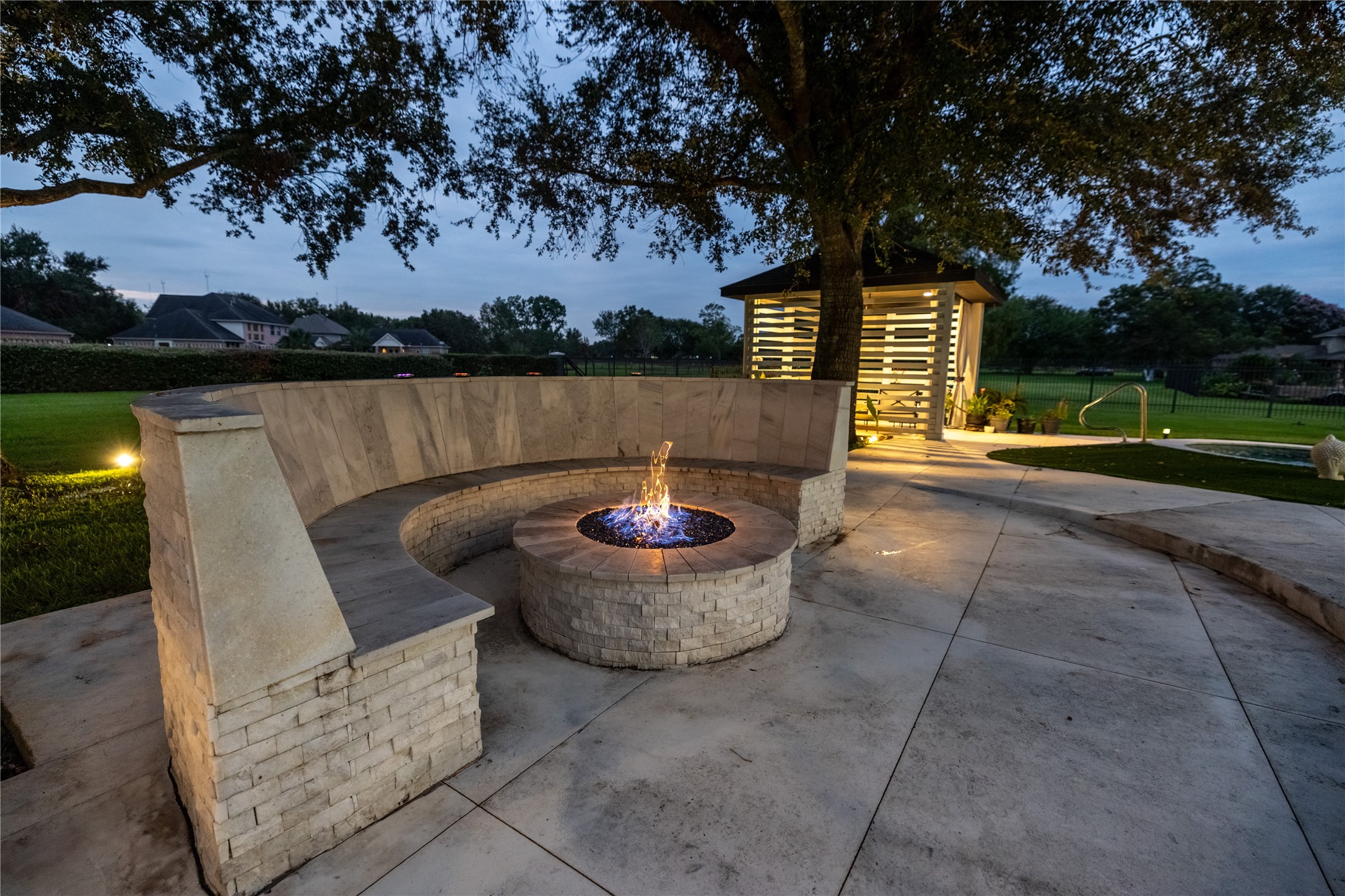 4002 Silver Ridge Boulevard Missouri City, TX 77459 - Photo 44 of 50 This is an elegant outdoor space featuring a circular fire pit with bench seating, perfect for entertaining. The area is complemented by a modern, well-lit structure and beautifully landscaped grounds, all set against a backdrop of mature trees and a clear view of the sky, ideal for enjoying evenings outdoors.