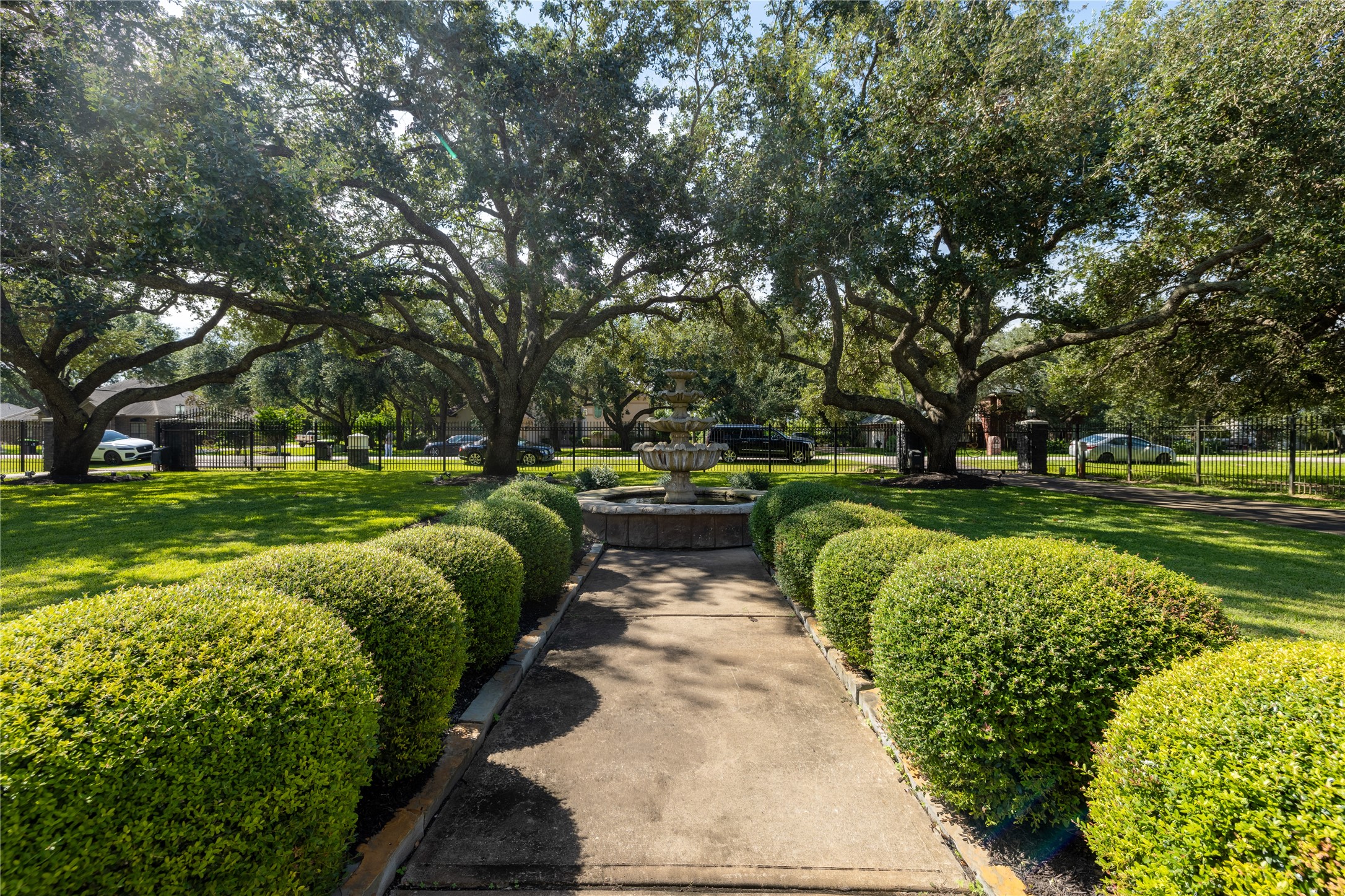 4002 Silver Ridge Boulevard Missouri City, TX 77459 - Photo 47 of 50 Well-maintained front yard with a symmetrical design of neatly trimmed hedges leading to an elegant fountain centerpiece, surrounded by mature, shady trees, providing a serene outdoor setting.