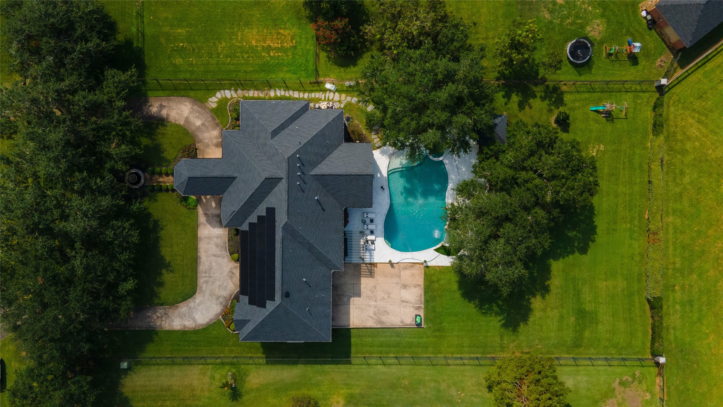 4002 Silver Ridge Boulevard Missouri City, TX 77459 - Photo 49 of 50 This aerial photo shows a spacious, multi-winged single-family home with a dark shingle roof, surrounded by a lush lawn. It features an in-ground pool with an adjacent patio area, a circular driveway in the front, and is nestled in a green setting with mature trees for privacy.