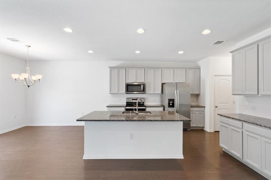6500 Routenburn Street Austin, TX 78754 - Photo 11 of 38 Kitchen featuring dark stone countertops, stainless steel appliances, a kitchen island with sink, dark wood-style floors, and hanging lights