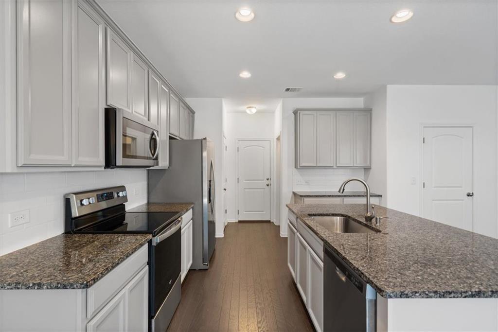 6500 Routenburn Street Austin, TX 78754 - Photo 10 of 38 Kitchen featuring stainless steel appliances, dark wood-style flooring, dark stone countertops, an island with sink, and recessed lighting