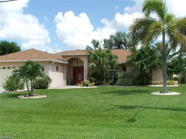 a view of a white house with a big yard and potted plants and palm trees