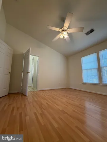 an empty room with wooden floor ceiling fan and windows
