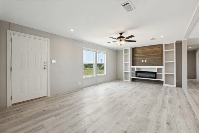 an empty room with wooden floor a ceiling fan and windows