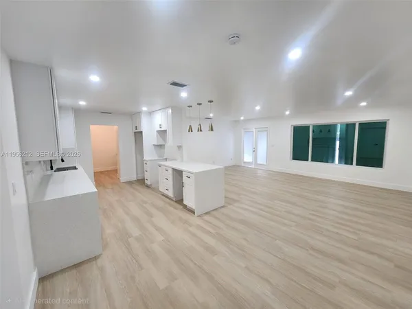 a large living room with stainless steel appliances kitchen island a sink a refrigerator and white cabinets with wooden floor