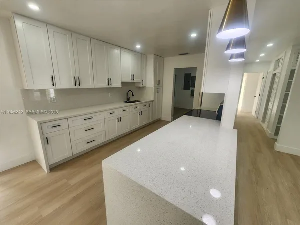 a large white kitchen with stainless steel appliances a large counter top a stove a microwave a sink and a refrigerator