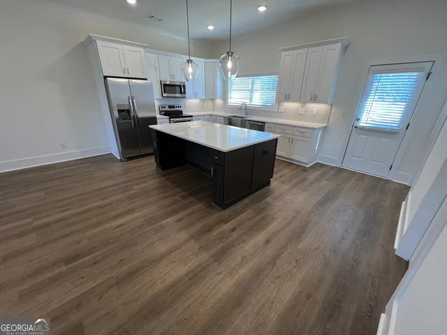 a large kitchen with kitchen island granite countertop a sink dishwasher a refrigerator and a stove with wooden floor