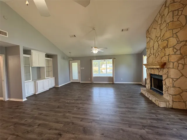 an empty room with wooden floor fireplace and windows