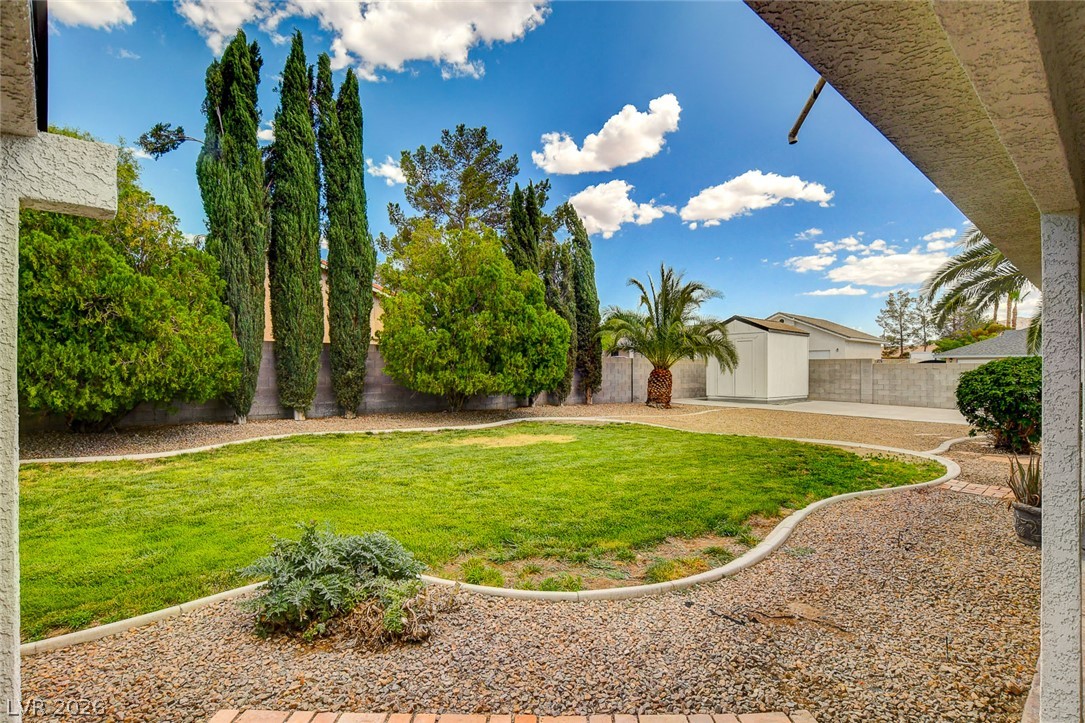 1810 Pinto Road Henderson, NV 89002 - Photo 43 of 53 A well-maintained yard featuring vibrant green lawn, gravel pathways, mature trees, and a practical storage shed.