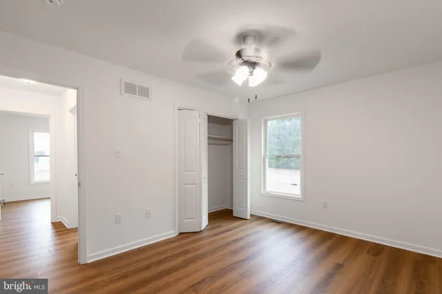 an empty room with wooden floor closet and windows