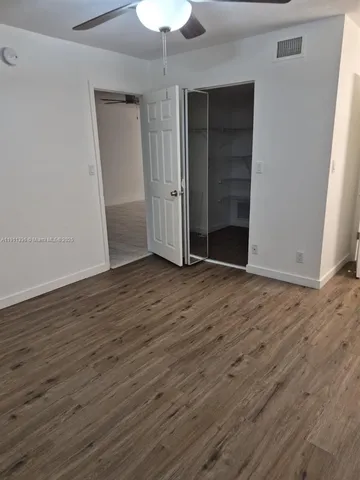 an empty room with wooden floor closet and windows