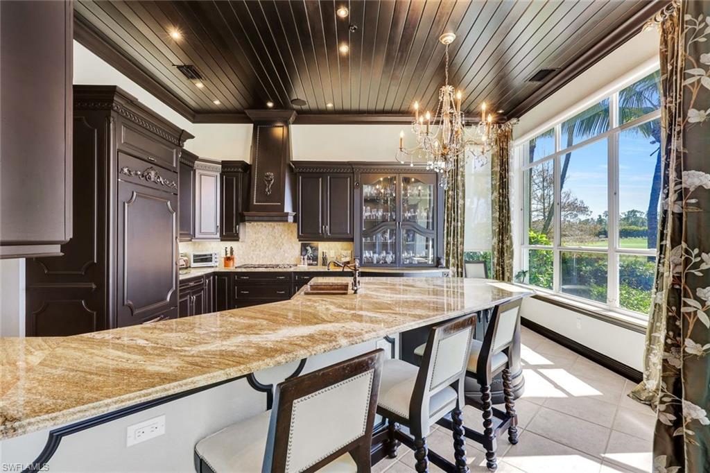 15516 Monterosso Lane, Unit 101 Naples, FL 34110 - Photo 13 of 31 Kitchen featuring a breakfast bar, backsplash, dark wood finish cabinets, a chandelier, and wooden ceiling