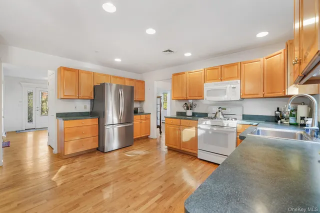 a kitchen with stainless steel appliances granite countertop a refrigerator a sink a stove a oven with white cabinets and wooden floor