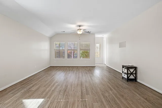 an empty room with wooden floor chandelier fan and windows