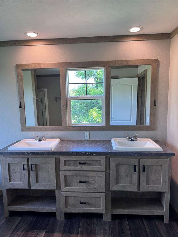 7268 Brangus Road Anna, TX 75409 - Photo 15 of 21 Dual vanity featuring a wood-finish cabinet with integrated storage, dark countertop, and two undermount sinks with chrome faucets