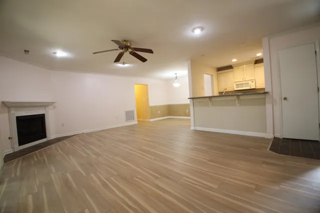an empty room with wooden floor kitchen view and a window