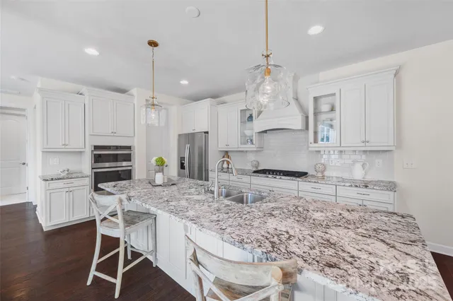 a kitchen with kitchen island granite countertop a stove a sink a oven and a refrigerator with wooden floor