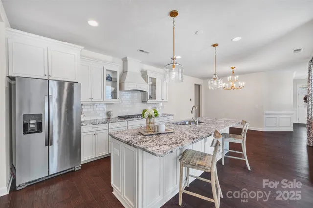 a kitchen with stainless steel appliances kitchen island granite countertop a dining table chairs and white cabinets