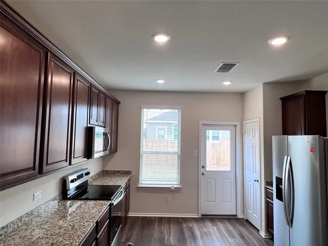 a kitchen with stainless steel appliances granite countertop a refrigerator a stove and a sink with wooden floor