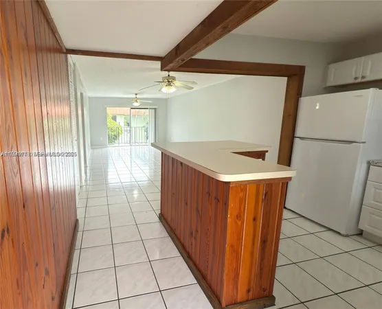 a view of a refrigerator in kitchen and an empty room with wooden floor