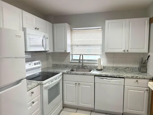 a kitchen with granite countertop white cabinets white appliances and sink