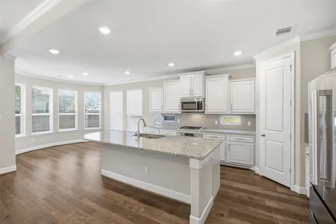 a large kitchen with stainless steel appliances granite countertop a stove a sink a refrigerator and white cabinets with wooden floor