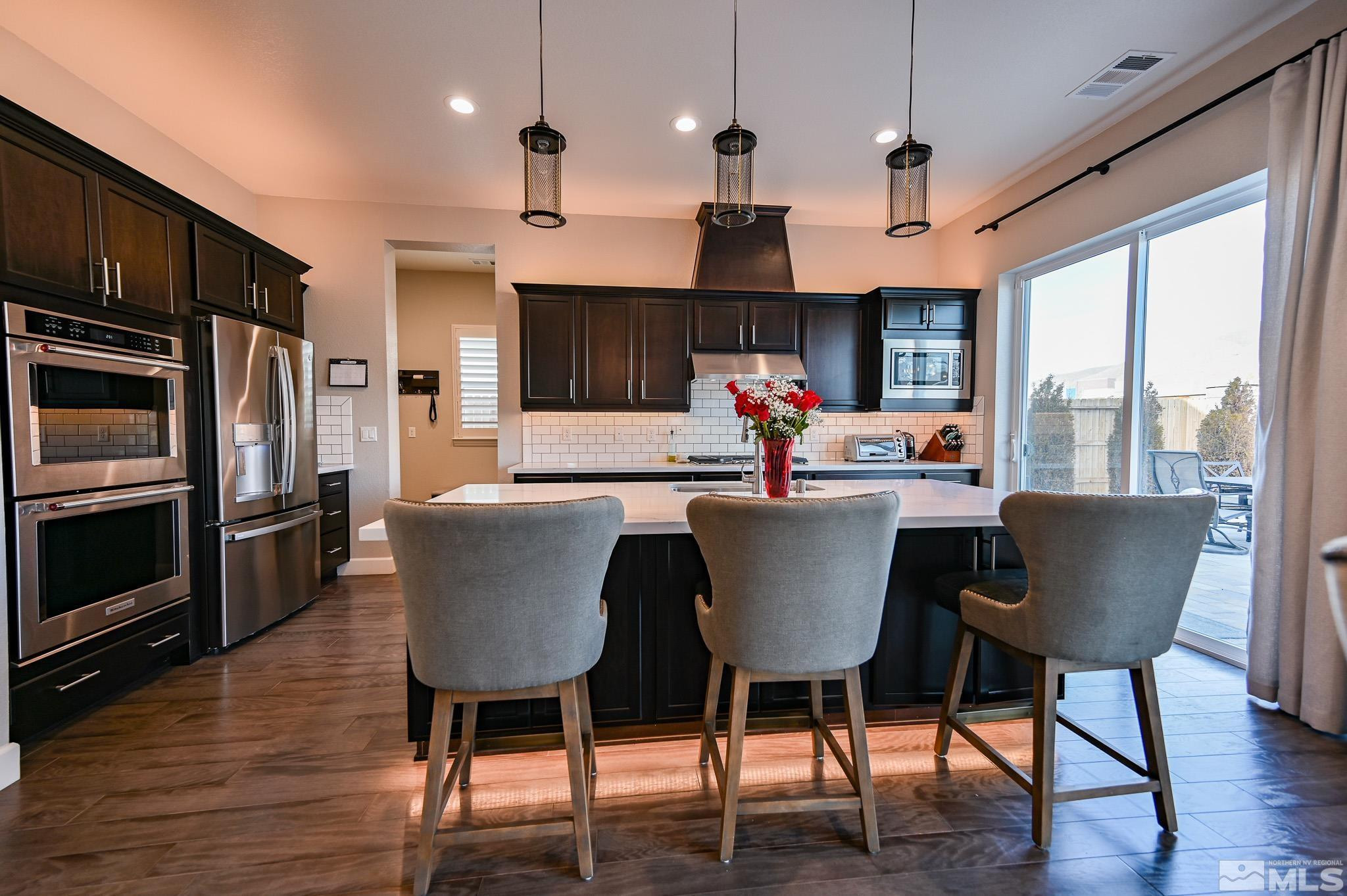 9330 Mayfair Way Reno, NV 89521 - Photo 8 of 40 a kitchen with stainless steel appliances granite countertop a stove a refrigerator a kitchen island a dining table and chairs with wooden floor