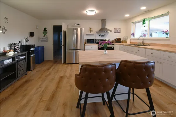 a kitchen with stainless steel appliances kitchen island granite countertop a refrigerator a stove a sink and a dining table with wooden floor