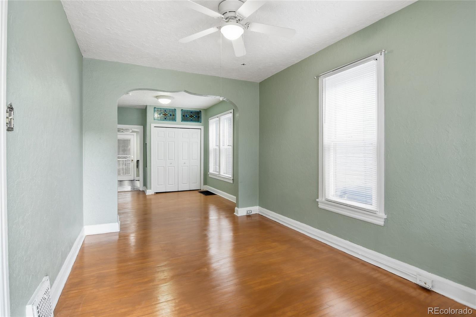 4424 Sherman Street Denver, CO 80216 - Photo 2 of 16 an empty room with wooden floor chandelier fan and windows