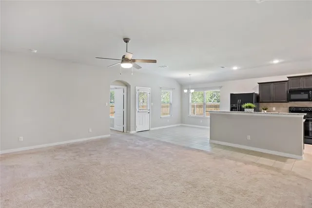a view of an empty room with kitchen and window