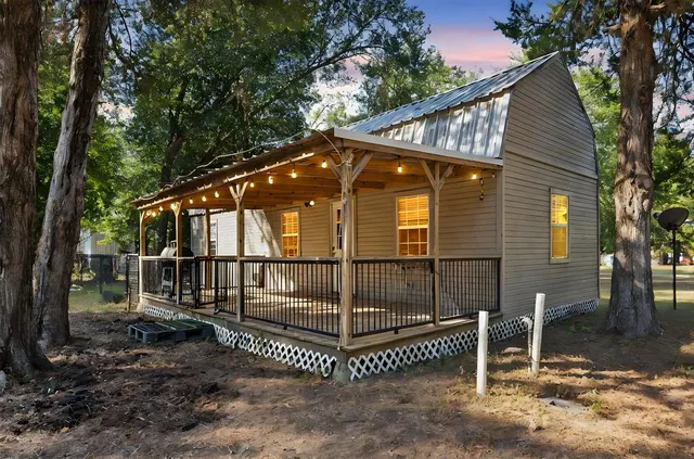 a view of a wooden house with a small yard and large trees