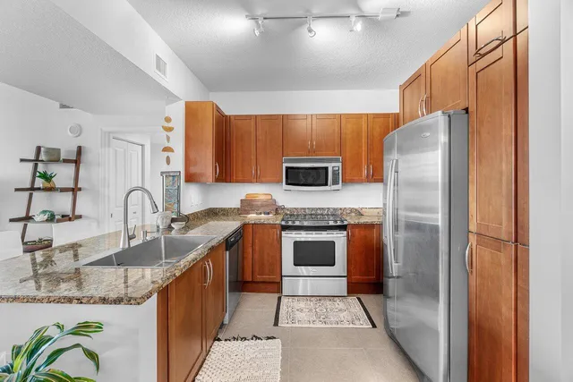 a kitchen with stainless steel appliances granite countertop a refrigerator a stove and a sink with wooden floors