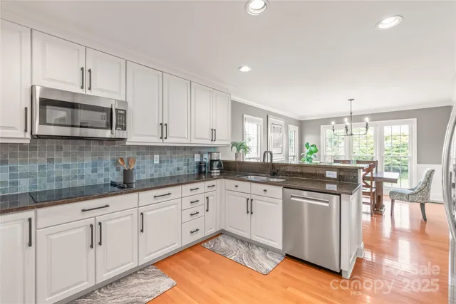 a kitchen with stainless steel appliances granite countertop a stove top oven a sink dishwasher and white cabinets with wooden floor