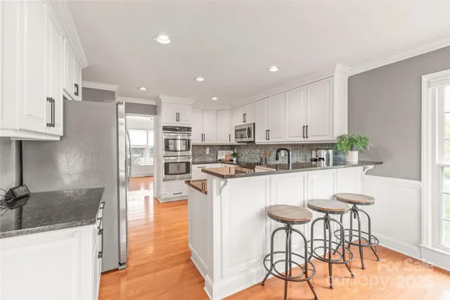 a kitchen with stainless steel appliances granite countertop a refrigerator a sink a stove a dining table and chairs